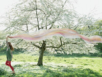 Girl with scarf skipping across meadow with flowering tree