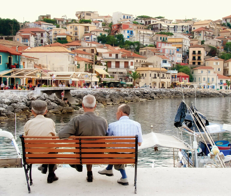 Three men sitting on a bench and looking out across a channel at a waterfront town